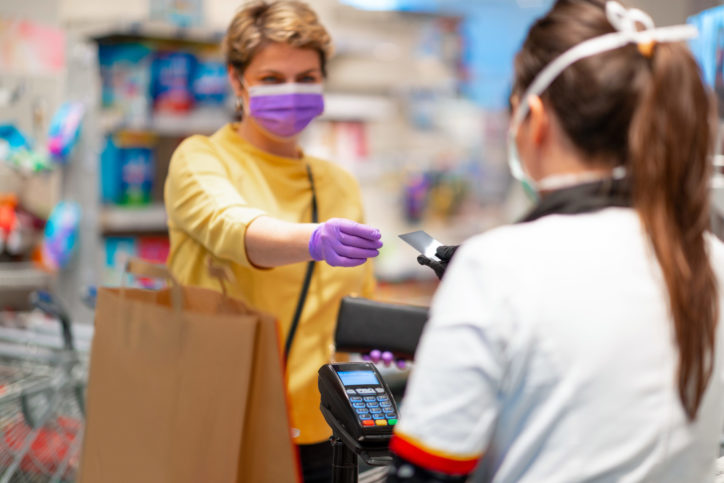 Woman with wallet wearing protective face mask and gloves to prevent viruses taking credit card back from cashier at cash register