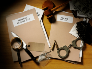 A brown desk is covered in police files, handcuffs, evidence, and a magnifying glass.